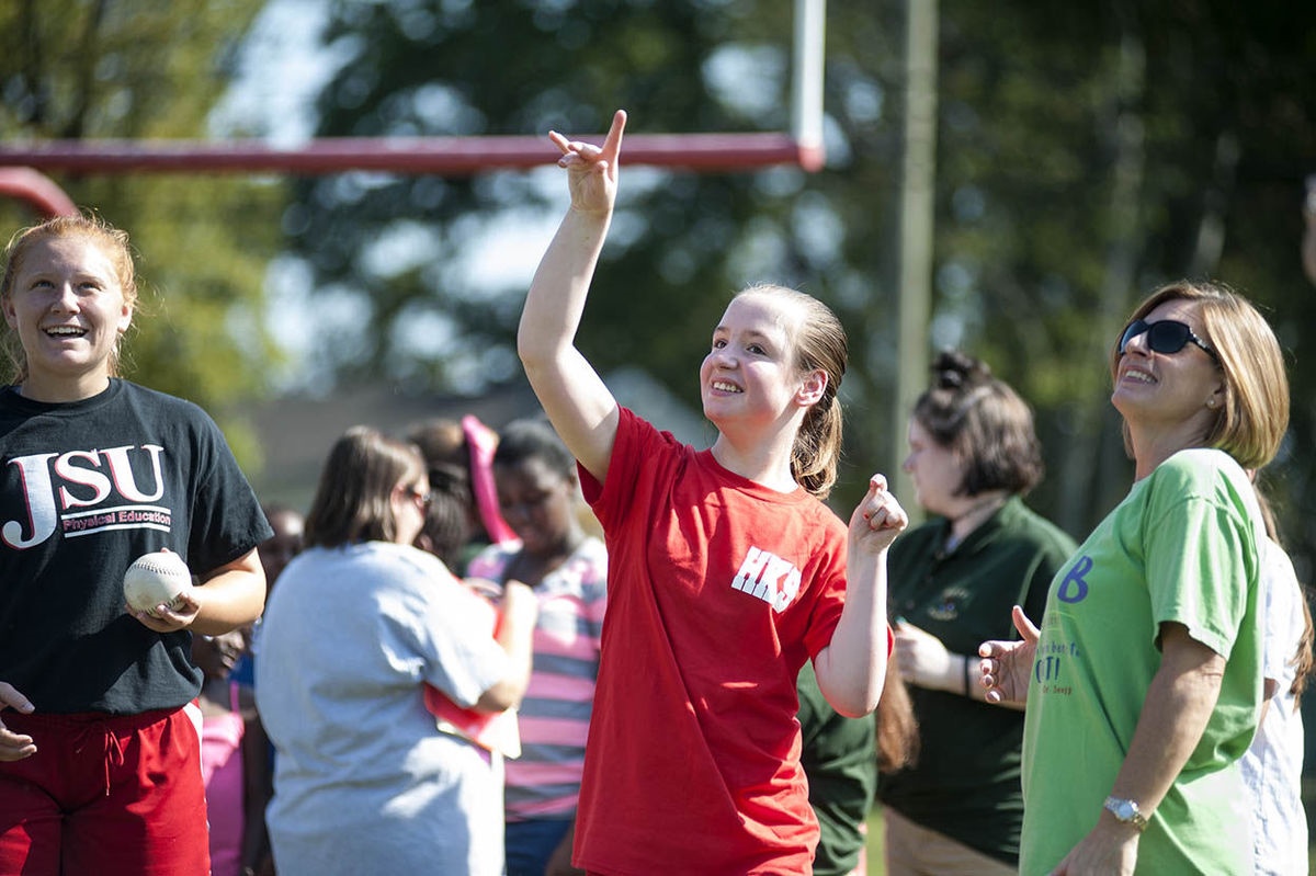 A female student participates in the softball throw as her teacher looks on. 